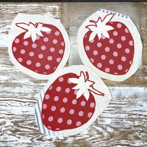 May include: Three fabric strawberry appliques featuring a red background with pink polka dots and a white stitched leaf top. Each strawberry shape is cut from off-white fabric, with one showing a blue and white striped edge detail.