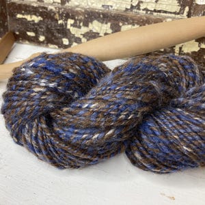 May include: A skein of yarn in a brown, blue, and white color combination. The yarn is soft and fluffy, and it is perfect for knitting or crocheting.