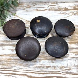 May include: A set of five round, dark brown wooden knobs with a smooth, matte finish. Each knob features a circular top surface and a slightly smaller base, showing signs of wear with minor surface scuffs and small areas of paint loss.