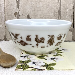 May include: A white milk glass mixing bowl featuring a brown printed pattern of various kitchen and farm-themed icons, including a rooster, an eagle, a coffee grinder, corn, and a tea kettle, arranged in a horizontal band around the exterior.