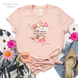 Proverbs 31:13 t shirt with images of pink, white and green knitting needles, crochet hooks, yarn and foliage.