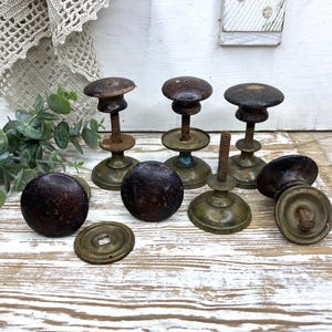 May include: A collection of vintage door knobs featuring dark brown, weathered wooden tops and tarnished brass bases. The set includes several upright knobs with threaded metal spindles and circular brass plates, showing signs of age and patina.