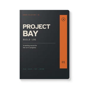以下が含まれることがあります： 右側に縦のオレンジ色のストライプが入った黒いノートで、Project Bay Build Logというタイトルが記されています。表紙にはGarage Collection / 01、A working record for the car in progress、Plan / Build / Test / Refineという白い文字が印刷されています。