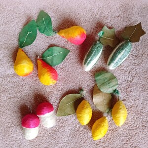 Könnte beinhalten: Eine Sammlung kleiner, handgefertigter Obst- und Gemüseornamente aus gewickelten Fasern. Das Set enthält zwei gelb-rote Birnen, zwei grün-weiß gestreifte Gurken, zwei rot-weiße Pilze sowie drei leuchtend gelbe Zitronen mit grünen Blättern.