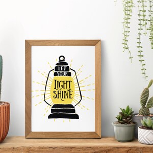 May include: A framed print with a black silhouette of a lantern with the text "Let your light shine" in yellow lettering.