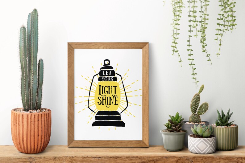 May include: A framed print with a black silhouette of a lantern with the text "Let your light shine" in yellow lettering.