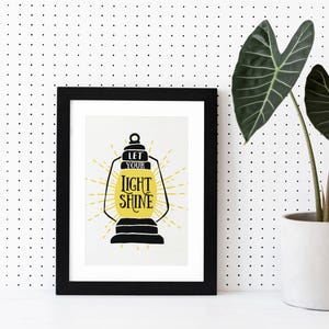 May include: Black framed print with a yellow and black lantern illustration and the text "Let your light shine".