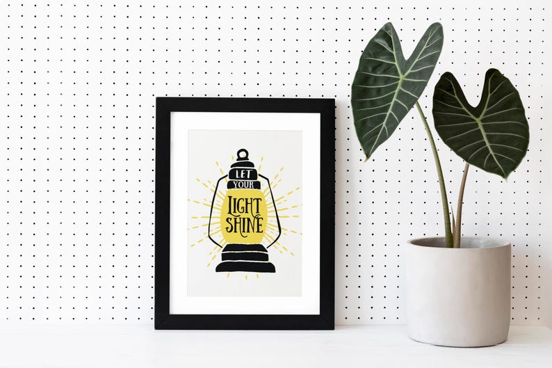 May include: Black framed print with a yellow and black lantern illustration and the text "Let your light shine".