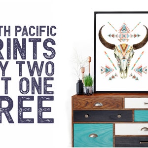 May include: A framed art print featuring a watercolor illustration of a bull skull with geometric patterns in shades of teal, orange, and beige. The artwork is displayed on a wooden dresser with various drawers. Text on the left reads "SOUTH PACIFIC PRINTS BUY TWO GET ONE FREE."