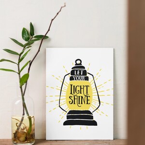 May include: A white printable poster with a black silhouette of a lantern with a yellow sunburst behind it. The text on the poster reads "Let your light shine."