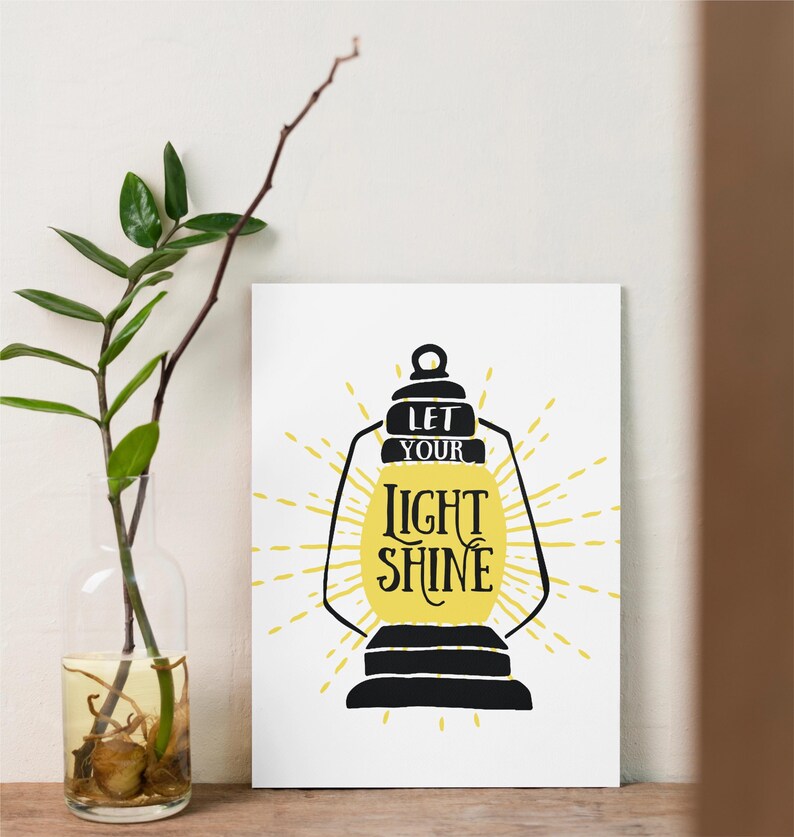 May include: A white printable poster with a black silhouette of a lantern with a yellow sunburst behind it. The text on the poster reads "Let your light shine."