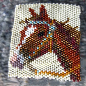 May include: A beaded horse head portrait with brown, white, orange, gold, and blue beads. The horse's eye is black and the background is white.