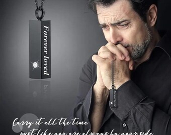 May include: A black rectangular pendant necklace featuring the engraved text Forever loved and a small embedded clear stone. The pendant hangs from a matching black chain, showcasing a sleek design with a polished finish and clean lines.
