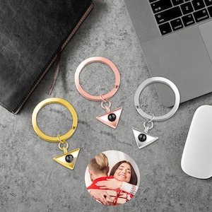 May include: Three gold keychains with a triangle charm featuring a black stone in the center. The keychains are on a gray surface.