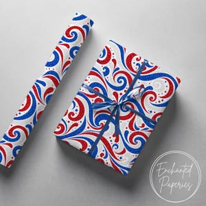 May include: A roll of wrapping paper and a rectangular gift box wrapped in the same paper, featuring a white background with swirling red and blue glitter patterns. The gift box is tied with a dark blue ribbon. The text Enchanted Paperies is visible.