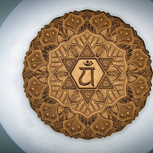 May include: A wooden mandala with intricate details and a central symbol of "DHA" in a geometric pattern. The mandala is brown and black and has a circular shape.