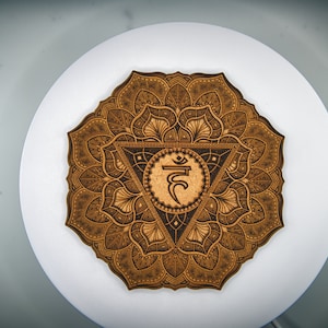 Könnte beinhalten: Ein Holzmandala mit einem braunen und schwarzen Design, das das Symbol für das Sakralchakra, "Svadhisthana", in der Mitte zeigt.