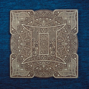 May include: A wooden plaque with an intricate design featuring the astrological symbol for Gemini. The design is detailed and includes a variety of swirls and patterns.