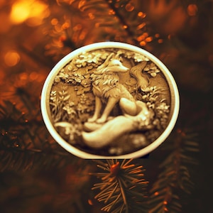 May include: A round, gold-colored ornament featuring a detailed, three-dimensional sculpture of a fox sitting in a forest setting.