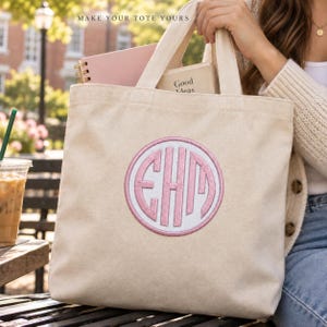 A woman holds a cream canvas tote with a white circular patch, Pale Pink monogram initials and a matching border. Books fill the tote. Heading: Make your tote yours.