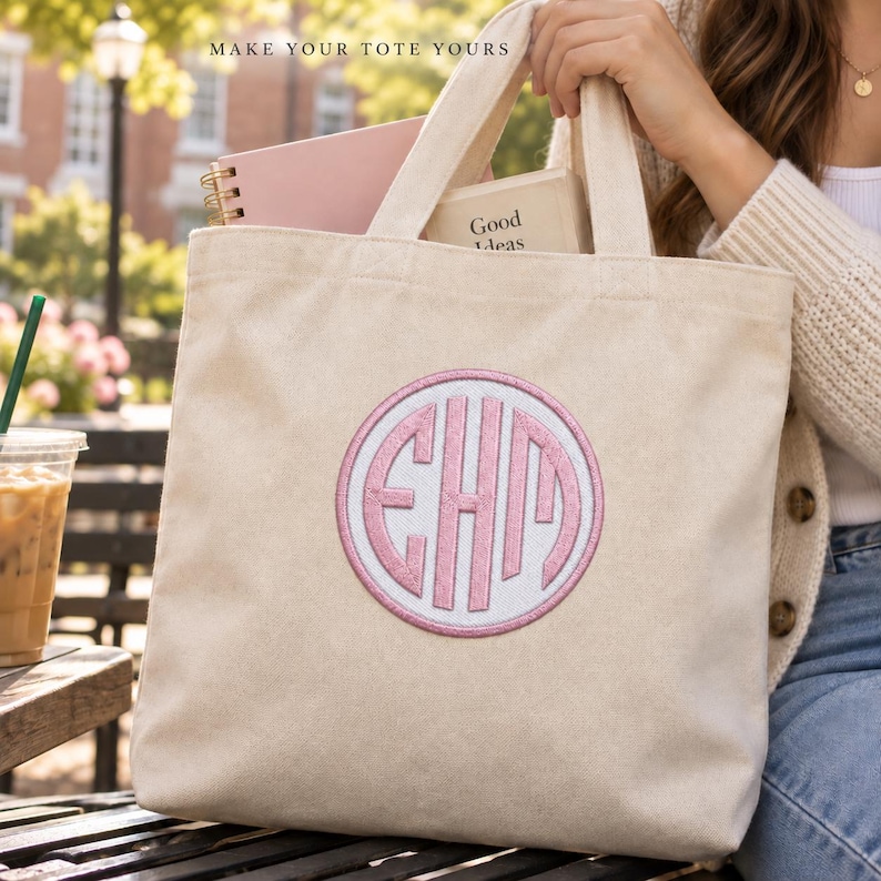 A woman holds a cream canvas tote with a white circular patch, Pale Pink monogram initials and a matching border. Books fill the tote. Heading: Make your tote yours.