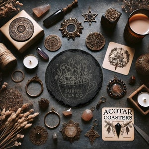 May include: A black slate coaster with a white design of a teacup filled with flowers and the text "Suriel Tea Co.". The coaster is surrounded by various decorative items, including candles, crystals, and a small wooden box.