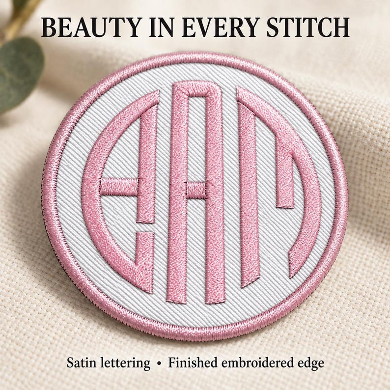 Close-up of a white twill monogram patch with Pale Pink satin lettering and a matching embroidered circular edge. Individual stitches and diagonal fabric texture are visible. Heading: Beauty in every stitch.