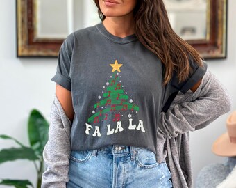 May include: A dark gray t-shirt with a green Christmas tree design featuring musical notes and the text "Fa La La".
