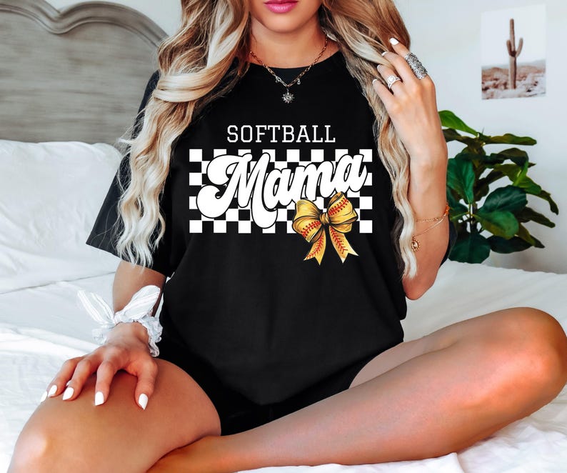 May include: Black t-shirt with a white and black checkered pattern and the text "Softball Mama" in white with a yellow softball bow.