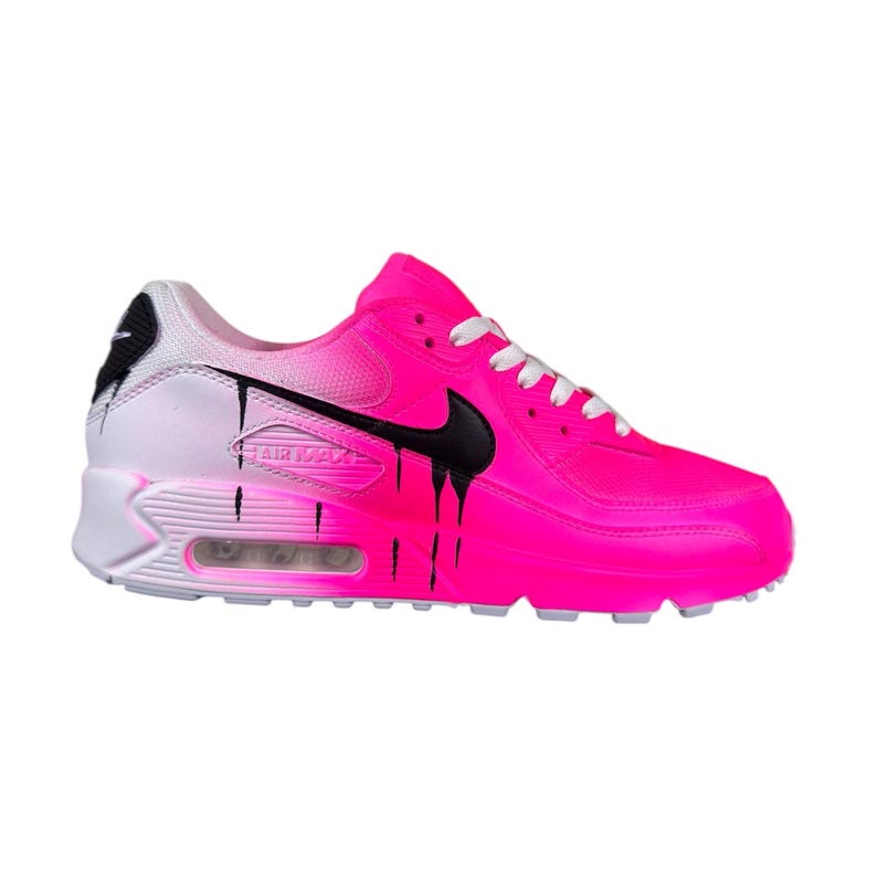 May include: Bright pink athletic shoe with black dripping paint design. The shoe features a black Nike swoosh and white laces. The heel is white with a black accent. The sole is white and gray. The words "AIR MAX" are visible on the side.
