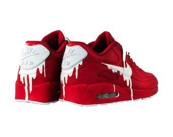 May include: A pair of red sneakers with white dripping paint accents. The sneakers feature the Nike Air Max logo on the heel and side. The design includes a white swoosh and white paint dripping down the sides.