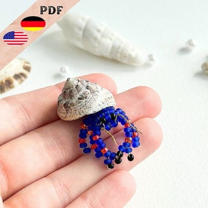 May include: A beaded hermit crab figurine with a blue and red body, black eyes, and a brown shell. The figurine is held in a hand.