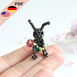 Könnte beinhalten: Eine kleine, geperlte Hasenfigur mit grünen und braunen Perlen. Der Hase hält eine rosa Blume mit einem grünen Stiel.
