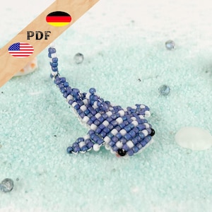 May include: A small whale shark figurine crafted from blue and white seed beads. The shark features a checkered pattern, two black bead eyes, side fins, and a curved tail. The structure is created using a bead weaving technique with visible thread.