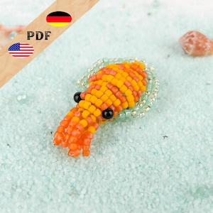 May include: A beaded squid figurine crafted from small orange and yellow glass beads with two prominent black bead eyes. The squid features a rounded mantle and multiple tentacles, accented by a translucent light green beaded border.