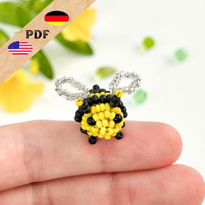 Puede incluir: Figura de abeja hecha a mano con cuentas amarillas y negras, alas plateadas y ojos negros. La palabra "PDF" es visible en la imagen, junto con las banderas de Estados Unidos y Alemania.