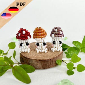 May include: Three beaded mushroom figurines with different colored caps. The mushrooms are white with black eyes and pink cheeks. The caps are red, orange, and purple.