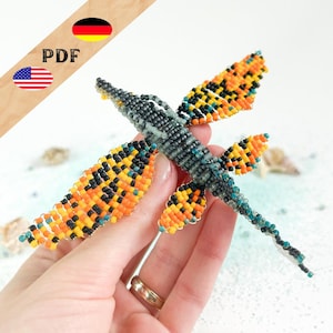 Könnte beinhalten: Eine Perlen-Libellen-Skulptur mit orangefarbenen, schwarzen und gelben Flügeln. Der Körper ist grau und türkis. Die Flügel bestehen aus kleinen Perlen. Das Bild enthält den Text "PDF" und die Flaggen der Vereinigten Staaten und Deutschlands.