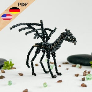 May include: Black beaded dragon figurine with wings outstretched. The dragon is standing on a white surface with small green and brown stones.
