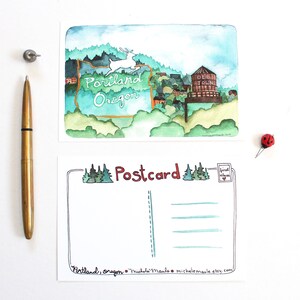 May include: A watercolor postcard featuring a stylized illustration of Portland, Oregon. The postcard includes a deer, a water tower, and the text "Portland Oregon". The back of the postcard has a space for writing a message and the text "Postcard".