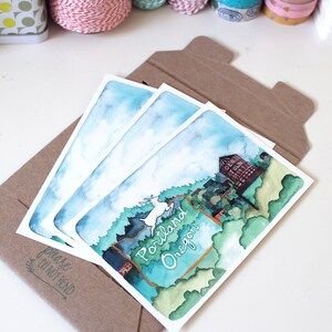 May include: Three watercolor postcards featuring a scenic illustration of a forest with a deer, a sign that reads "Portland Oregon", and a building that says "Old Town". The postcards are in a brown envelope with the words "Please Do Not Bend" printed on the front.
