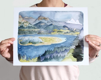 May include: A watercolour landscape painting on white paper featuring a blue lake with a central island, surrounded by dense green forests and layered mountain ranges in shades of blue, grey, and tan. The artwork displays fine ink line details.