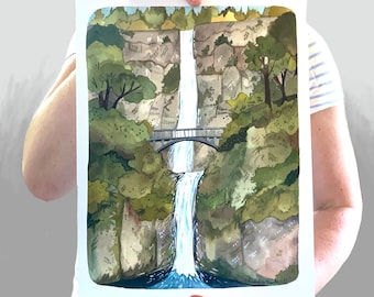 Peut inclure: Une peinture à l'aquarelle d'une cascade descendant d'une falaise rocheuse. Des arbres et des feuillages verdoyants luxuriants entourent la cascade, et un petit pont enjambe l'eau en haut. La peinture est encadrée de blanc.