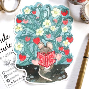 Può includere: Un adesivo stravagante raffigurante un topo che legge un libro rosso in mezzo a un campo di fragole con fiori bianchi. L'adesivo ha un bordo azzurro e include il nome dell'artista e i suoi social media.