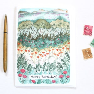 May include: A watercolour birthday card depicting a layered landscape with green, orange, and pink floral elements. The card includes the text "Happy Birthday!" and is accompanied by a gold pen and three vintage postage stamps.