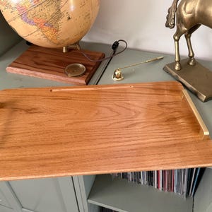 May include: A rectangular wooden serving tray with a light brown finish and gold-colored handles. The tray is displayed on a gray surface, with a globe and a brass horse statue in the background.