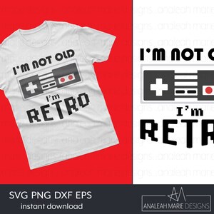 May include: A white t-shirt with a black and gray video game controller graphic and the text "I'm not old I'm retro".