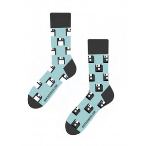 Może przedstawiać: Para niebieskich skarpet z czarnym wzorem dyskietek. Skarpety mają napis "WHATGEEKSNEED.COM" na dole.