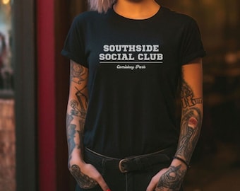 Puede incluir: Una camiseta negra con texto blanco que dice "Southside Social Club Comiskey Park". La persona que lleva la camiseta tiene tatuajes en los brazos.