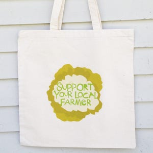 May include: A white canvas tote bag with a green and yellow graphic that says "Support Your Local Farmer".